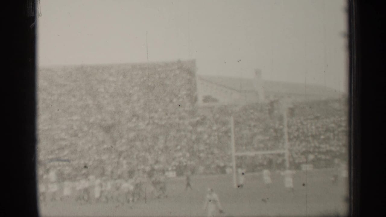 Football players run near the goalposts in front of crowded stadium seating.