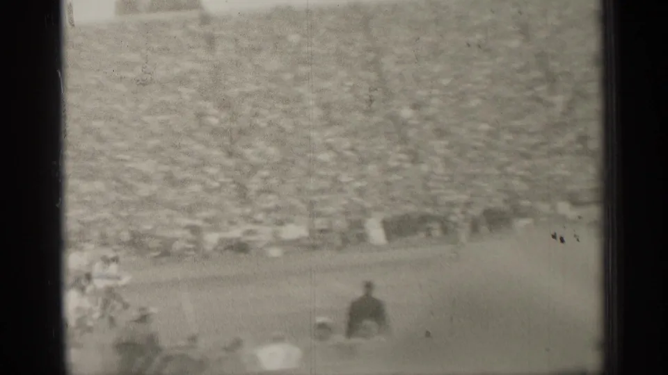 Soft, grainy 1944 San Francisco stadium view with a packed grandstand and small figures along the football field edge.