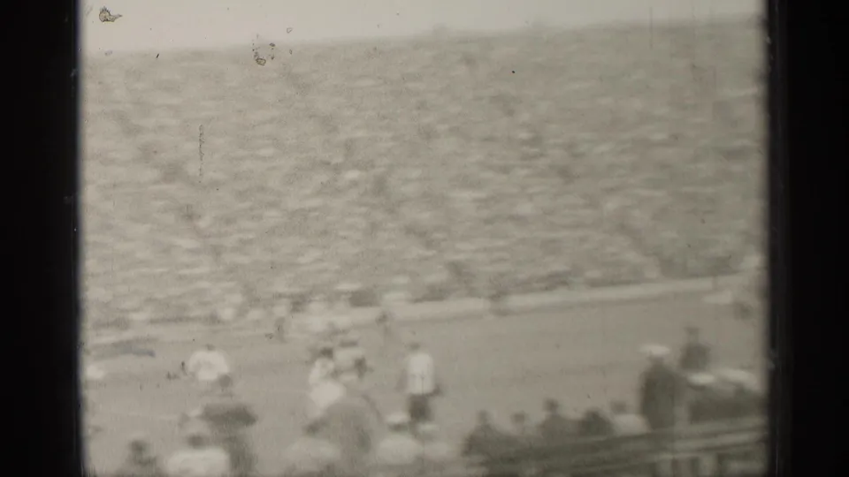 Distant home-movie frame of players moving down a San Francisco football field with a packed 1944 stadium crowd behind them.