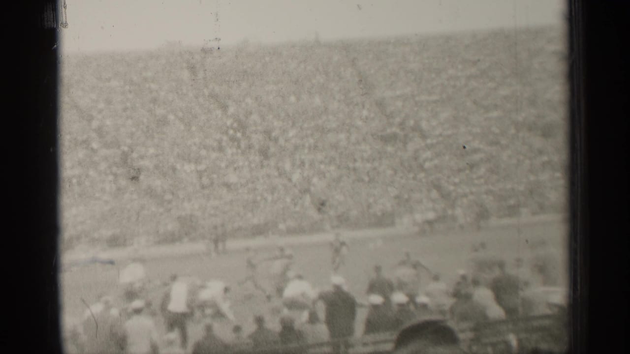 Distant football play in a crowded stadium with spectators in the foreground.