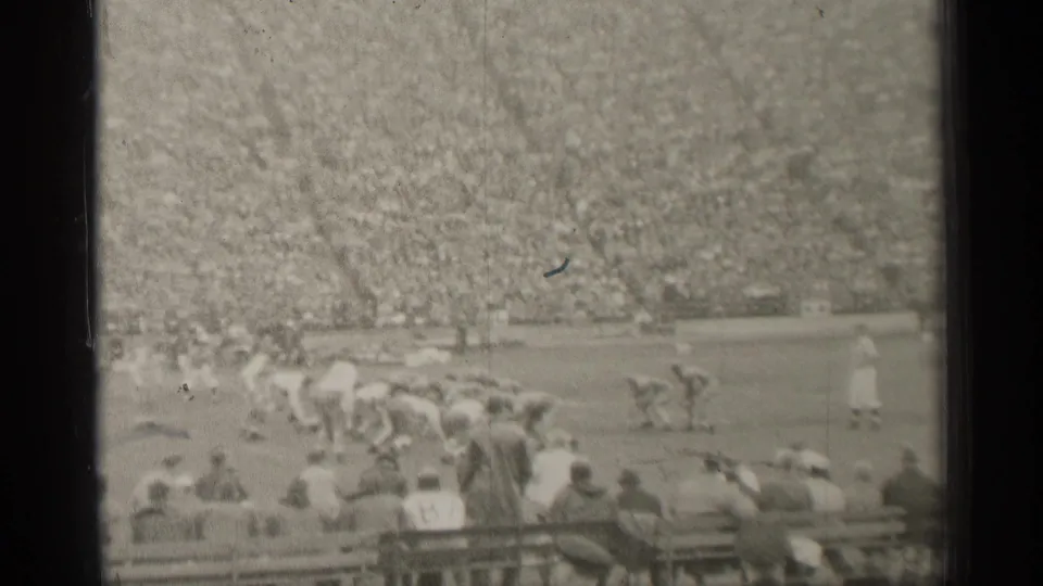 The 1944 San Francisco home-movie frame shows players lined near scrimmage, with foreground spectators watching from the stands.