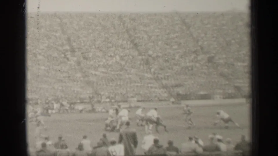 A wide 1944 San Francisco stadium frame shows football action, sideline figures, foreground viewers, and crowded seating.