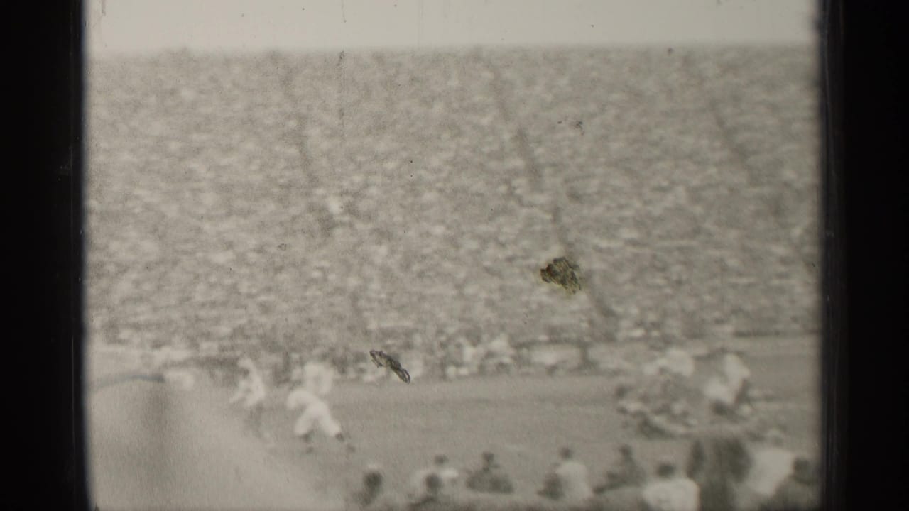 Black-and-white 8mm frame from a San Francisco football game, showing distant field action and a dense crowd in the stands.