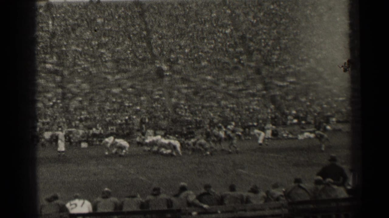 Football players line up near the sideline with a large crowd behind them.