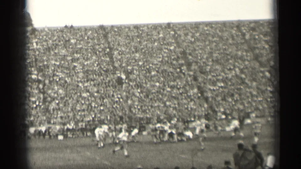 Black-and-white 8mm frame of football action in San Francisco, with players spread across the field and a large crowd in the stands.