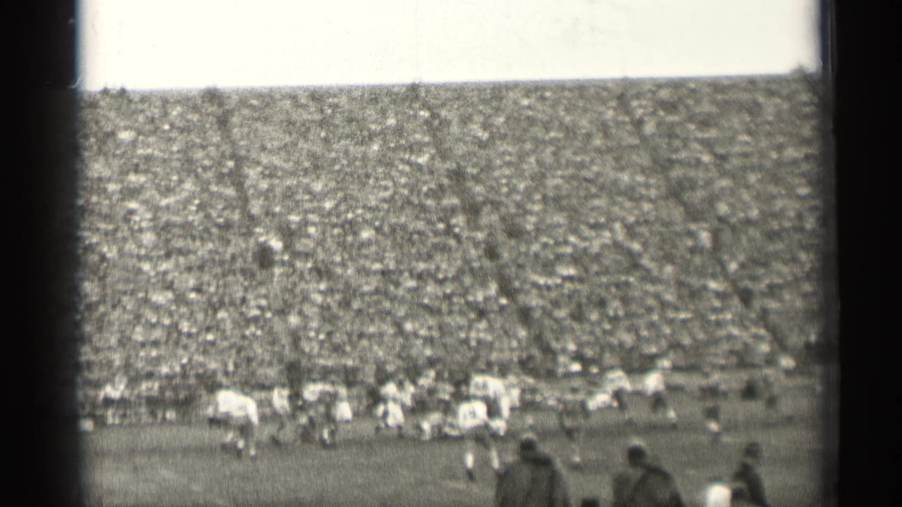 Football players on a field with a packed stadium crowd behind them.