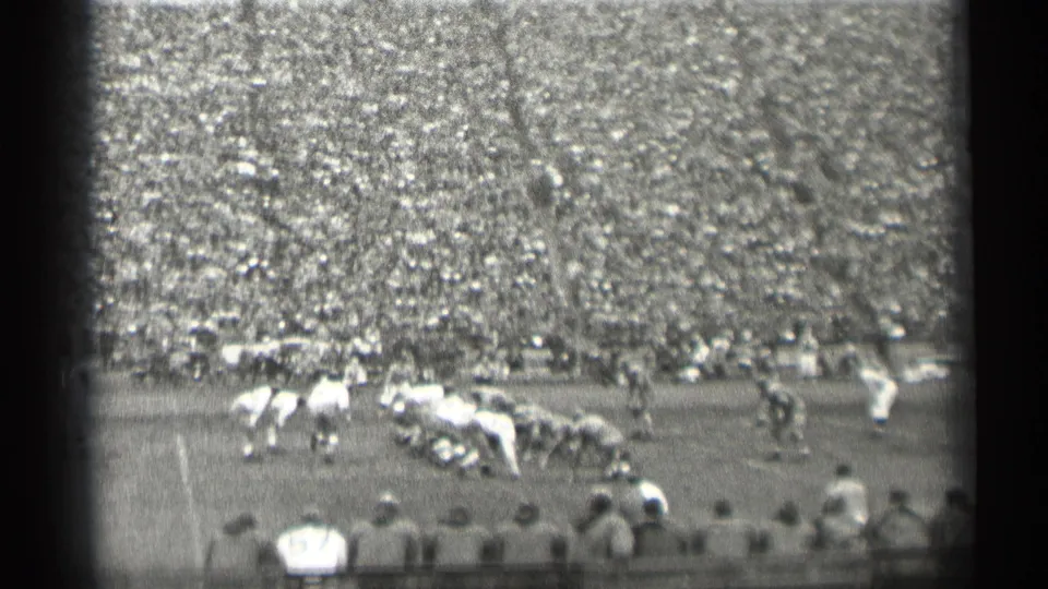 Football players appear set near the line of scrimmage in a 1944 San Francisco stadium, with sideline figures and a full grandstand behind them.