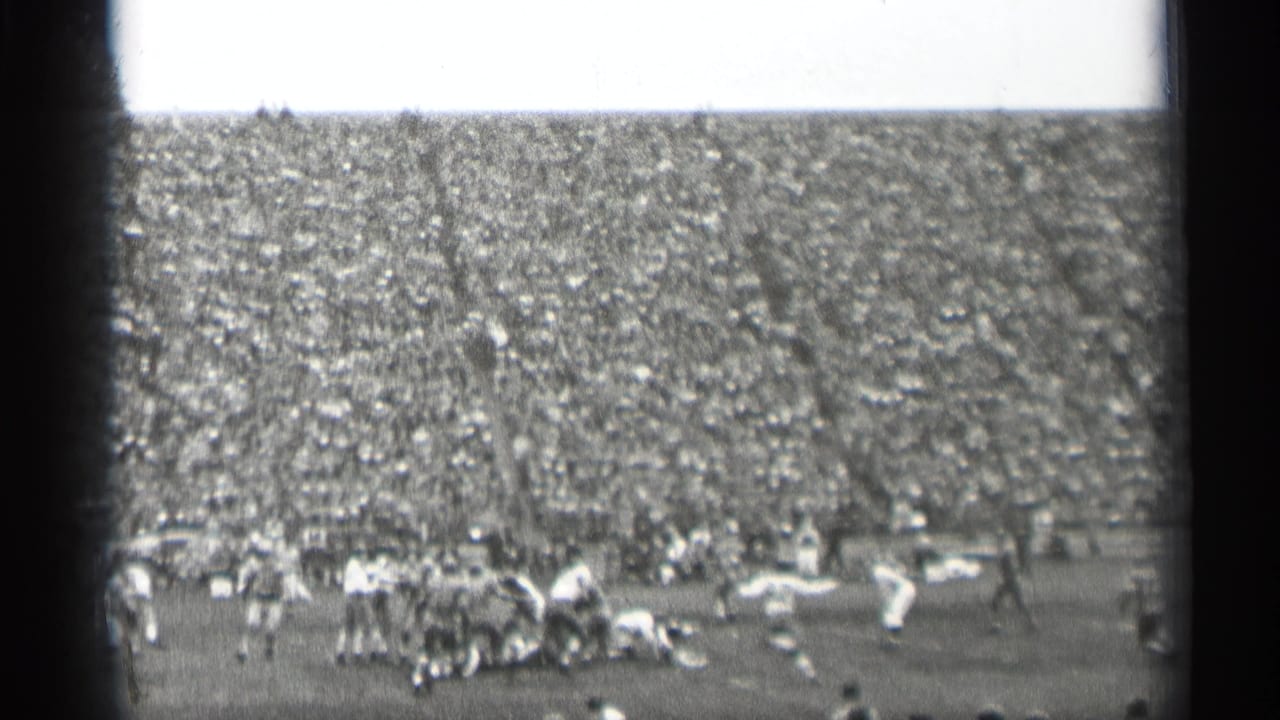 Football play on a field before packed stadium stands.