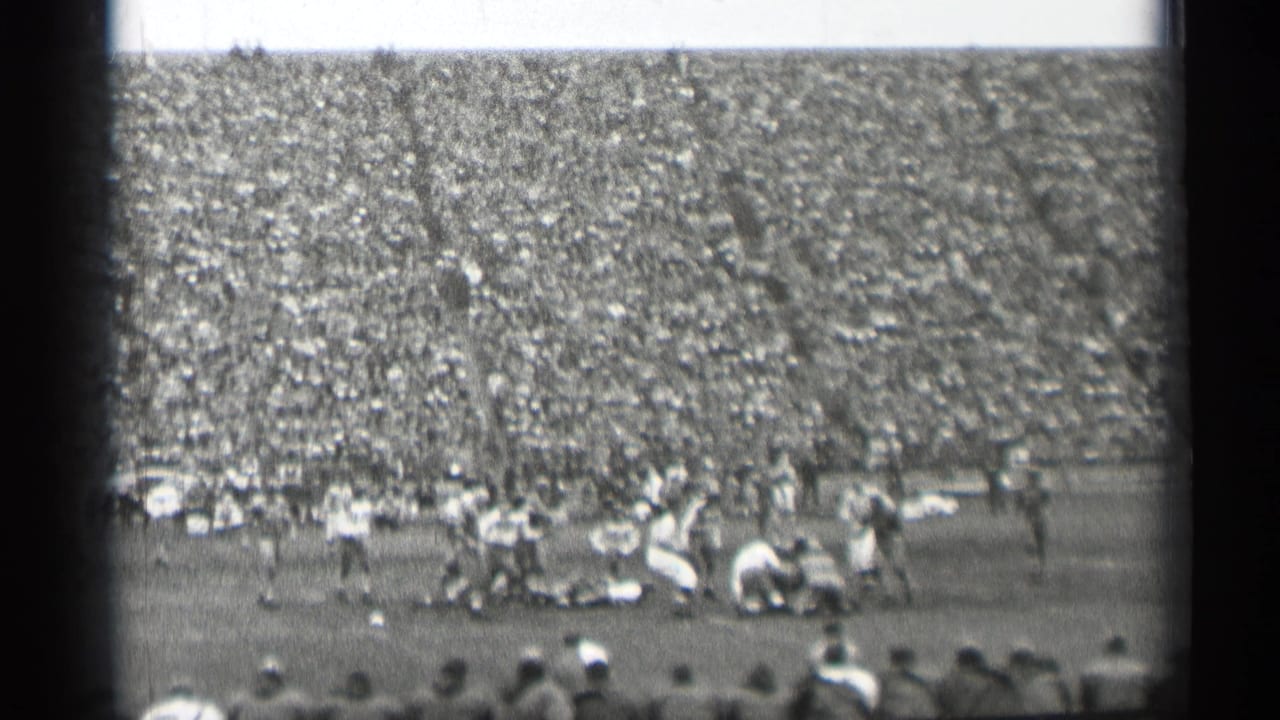 Football players collide near midfield with spectators in the stands.