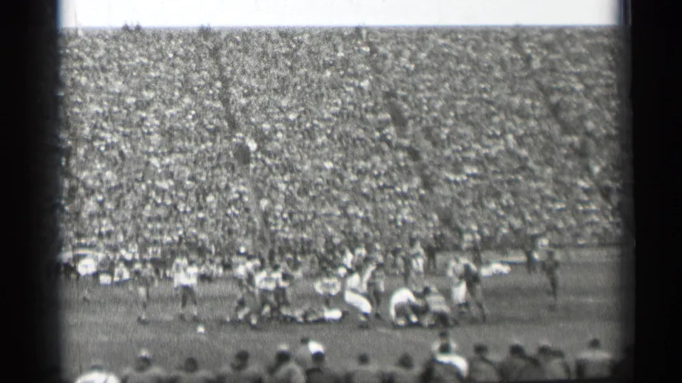 A football play unfolds in a crowded San Francisco stadium, with players in light and dark uniforms moving near the center of the field.