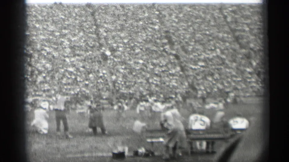 Sideline figures and seated players appear in front of a packed stadium during the 1944 San Francisco football game.
