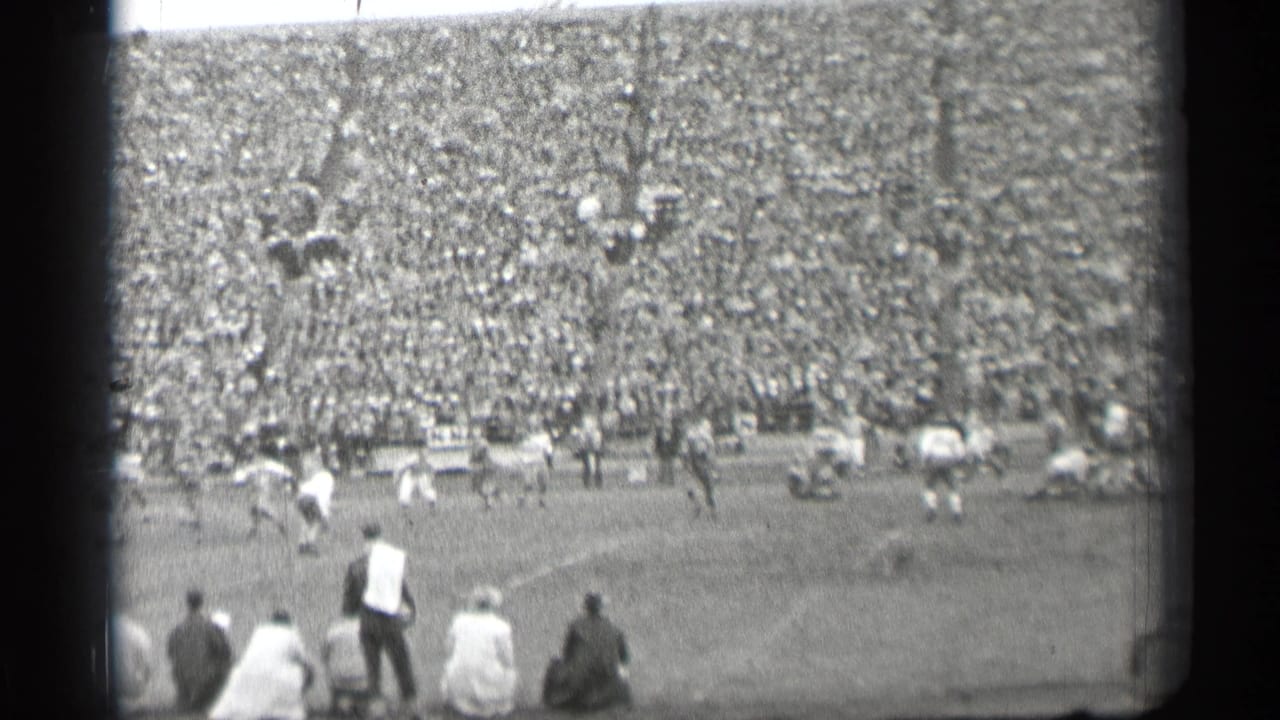 Football game seen from the stands with players on the field and a packed crowd behind them.