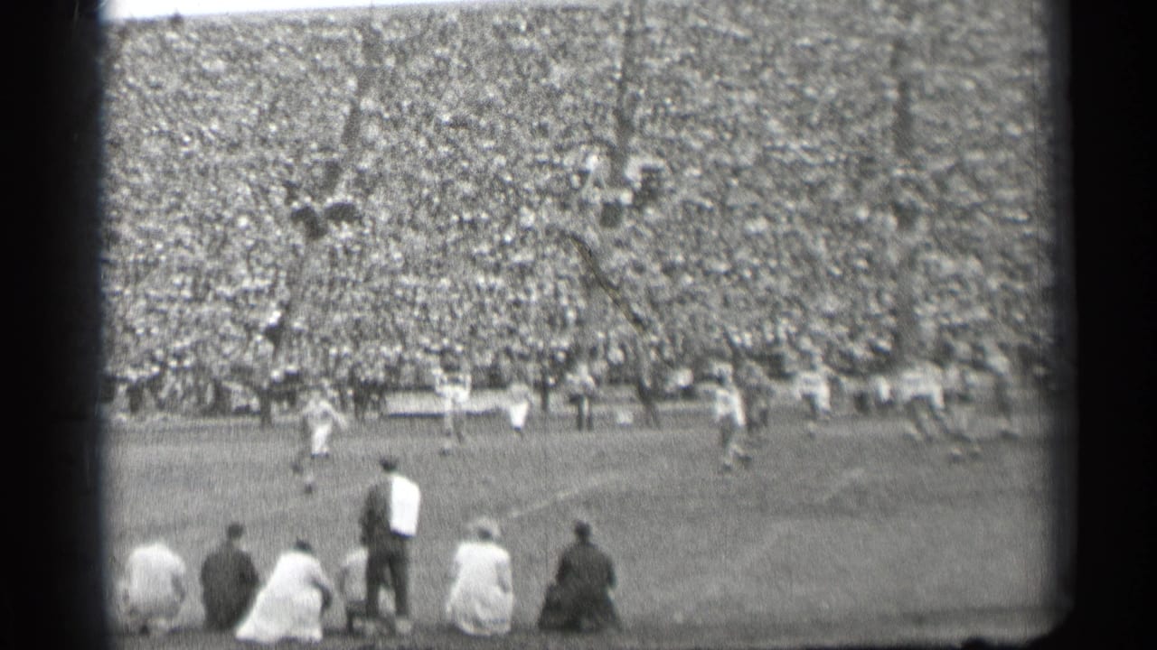High-angle 1944 San Francisco stadium view showing football players in motion, a dense crowd, and spectators seated near the camera.