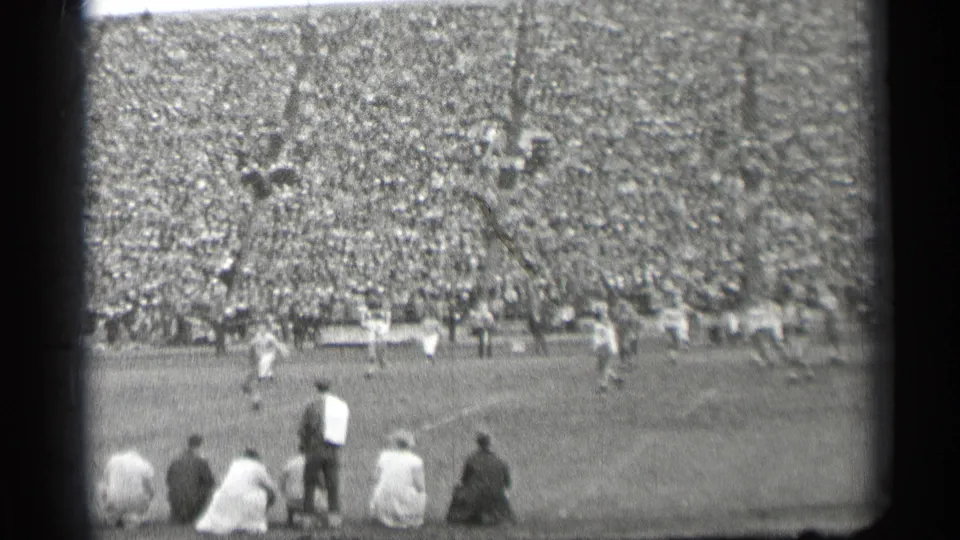 High-angle 1944 San Francisco stadium view showing football players in motion, a dense crowd, and spectators seated near the camera.