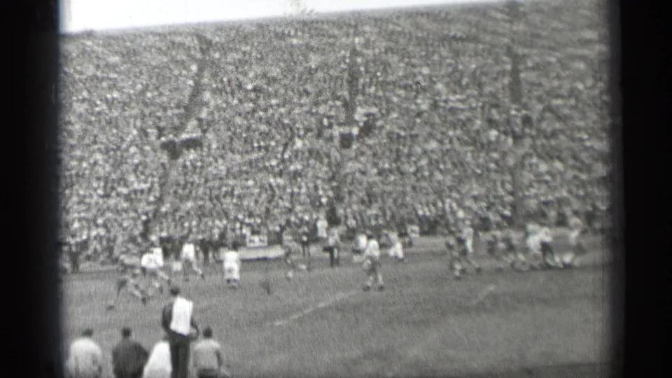 Wide 1944 San Francisco football stadium frame with distant players, seated and standing spectators, and a packed background crowd.