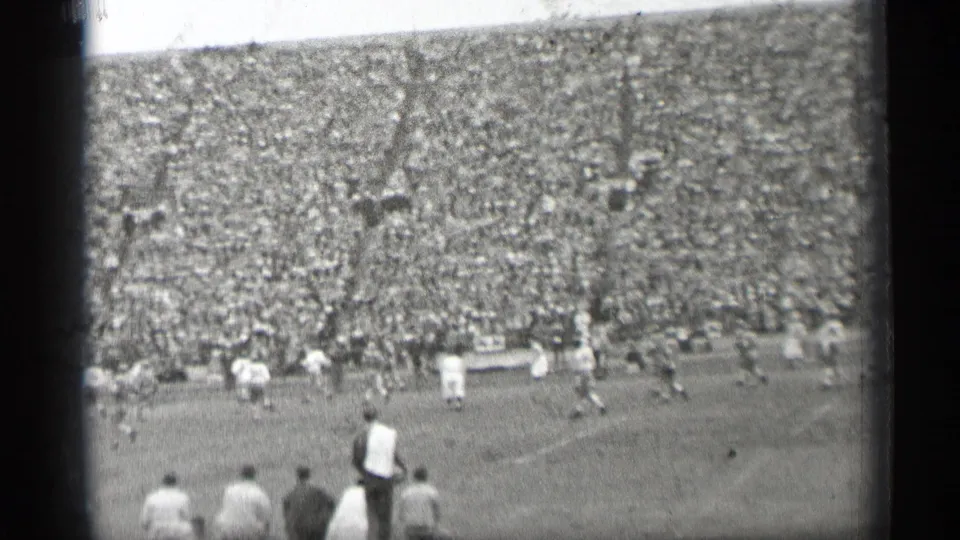 1944 San Francisco home-movie frame showing a football play from the stands, with light and dark uniforms and a dense crowd in the background.