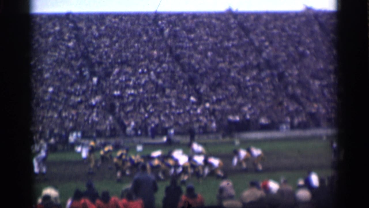 Distant 8mm frame of a football team formation in a San Francisco stadium, with spectators filling the background.
