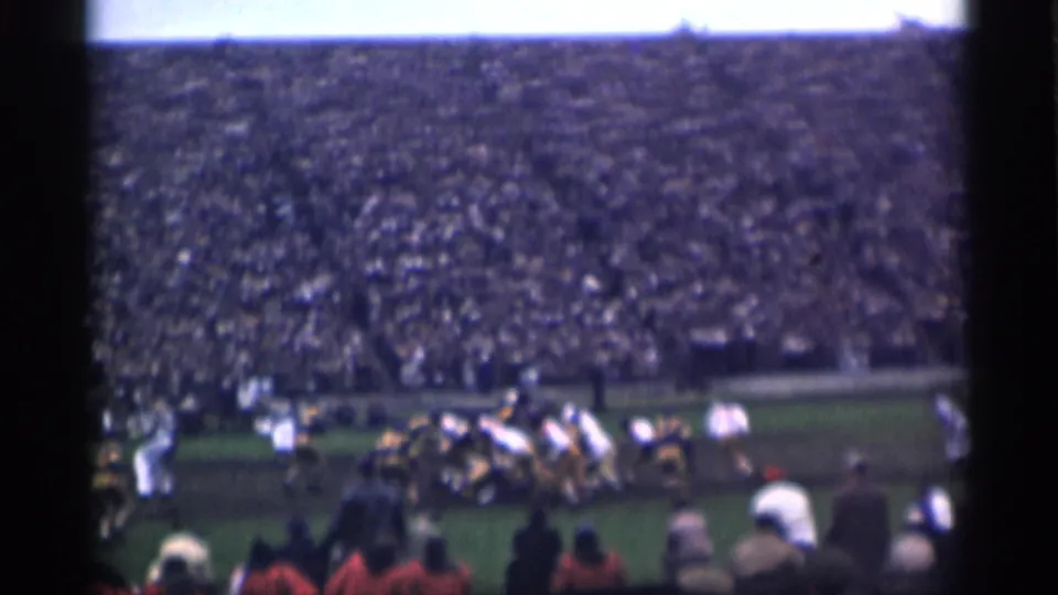 Home-movie view of football players preparing for a play in a crowded 1944 San Francisco stadium.