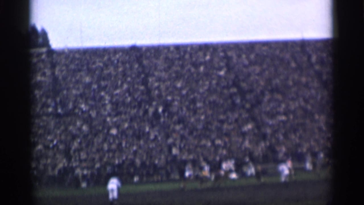 Players gather near the right side of a field with crowded stands behind.