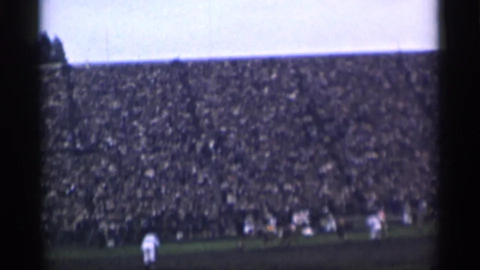 Distant 1944 San Francisco stadium view with players clustered during a sporting event before a full crowd.