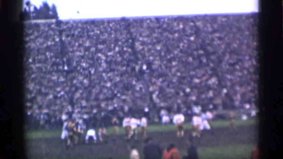 1944 San Francisco home-movie view of football players in white and dark uniforms on a field with a crowded grandstand behind them.