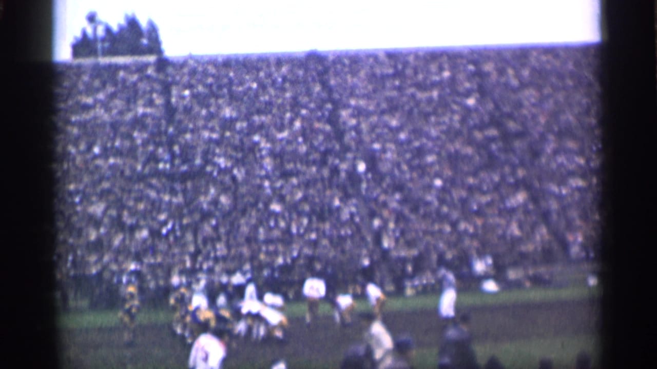 Distant 1944 San Francisco football action seen from the stands, with players converging near the center of the field and a large crowd behind them.