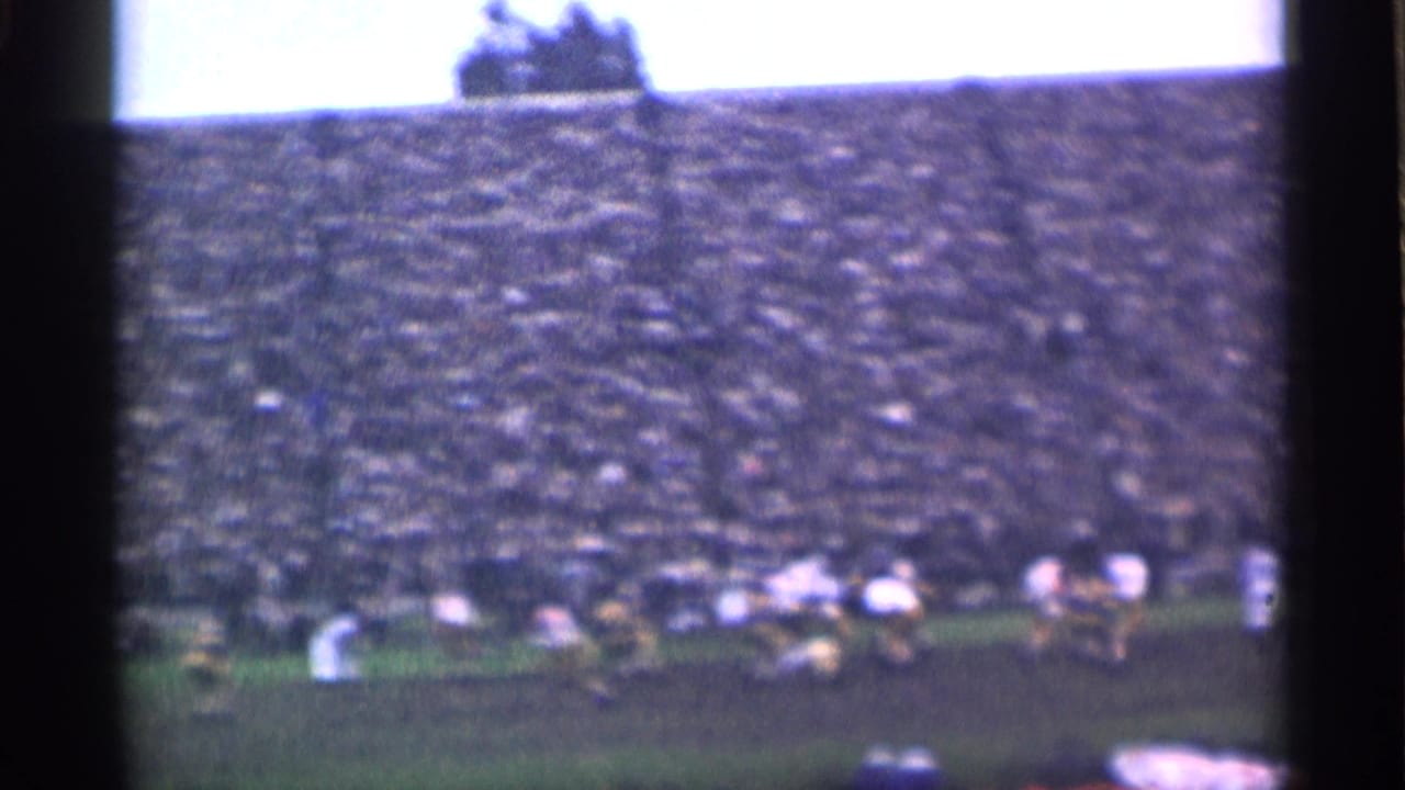 A college football play appears in progress on a muddy San Francisco field, filmed from the stands in soft 8mm color.