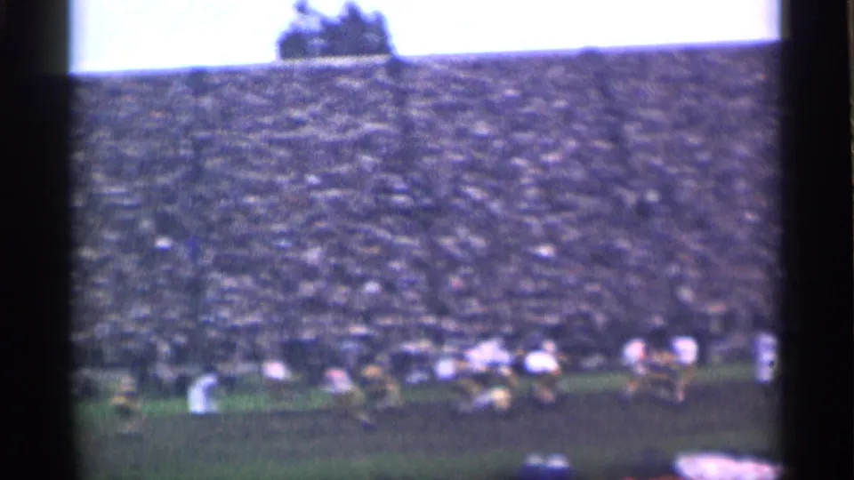 A college football play appears in progress on a muddy San Francisco field, filmed from the stands in soft 8mm color.