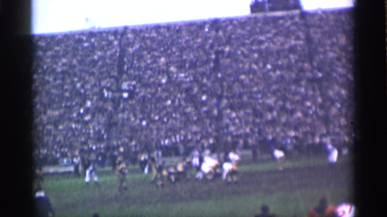 Wide 8mm view of the rugby match in San Francisco, with athletes in formation and a large seated crowd in the background.