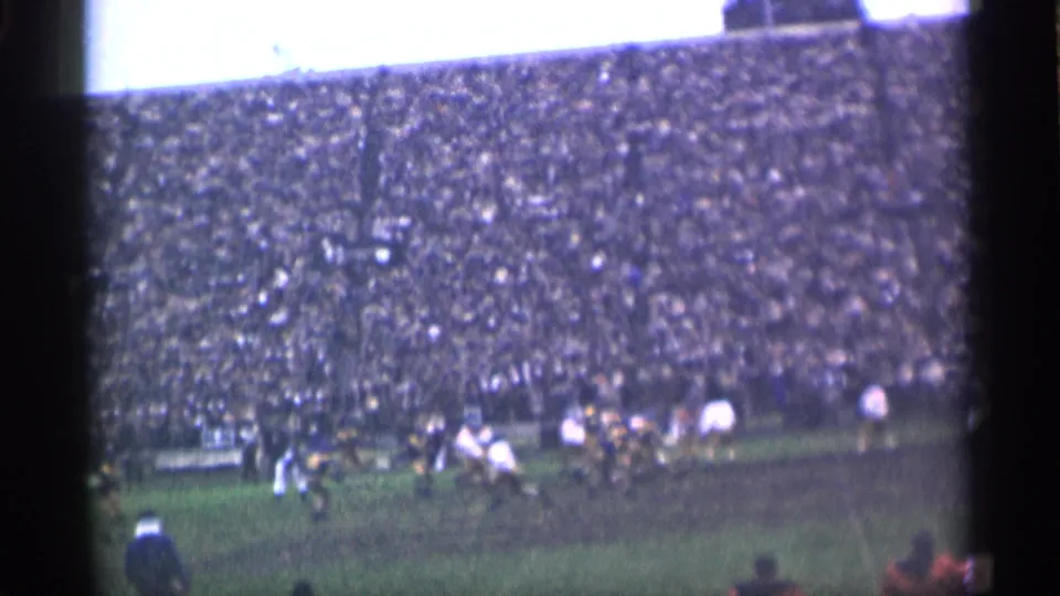 1944 home-movie frame from San Francisco showing players moving across a grassy field below a densely packed stadium crowd.