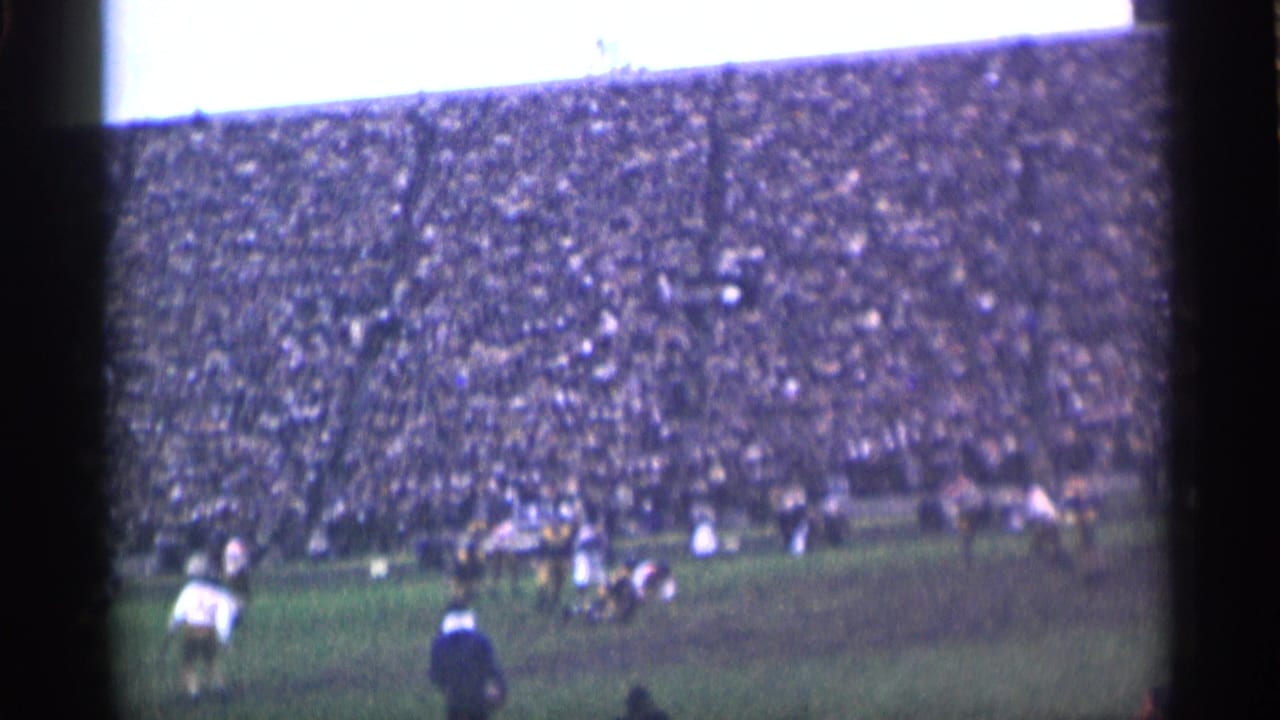 Football players line up on a field before a packed stadium crowd.