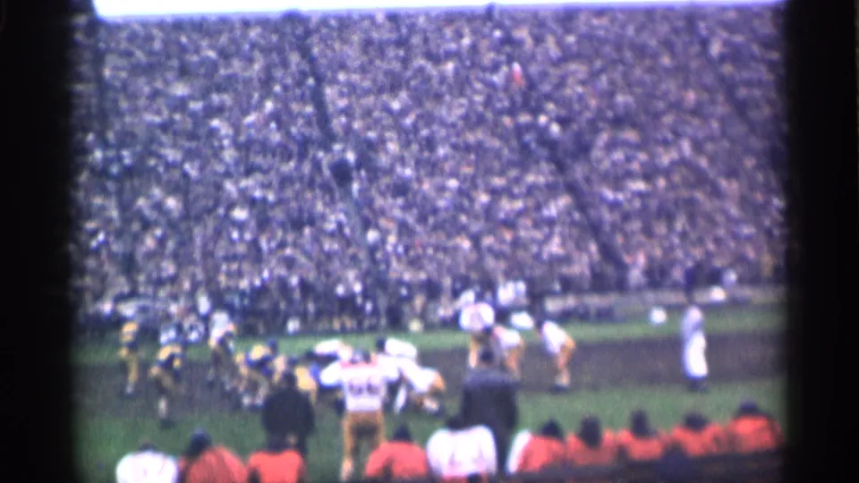 1944 San Francisco football game frame with players running during a play and spectators packed across the stadium seating.