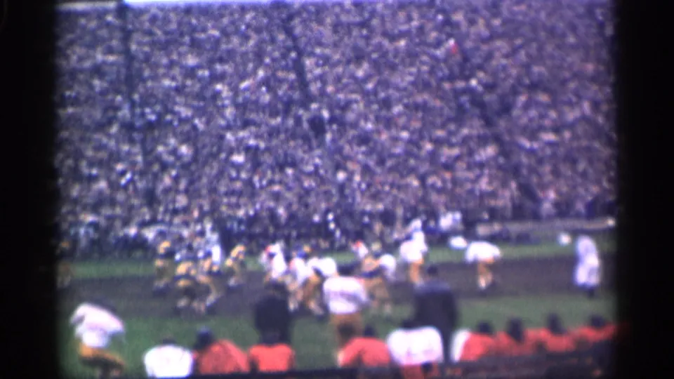 Home-movie view of a 1944 San Francisco football play, with linemen and backs on the field and spectators filling the stands.
