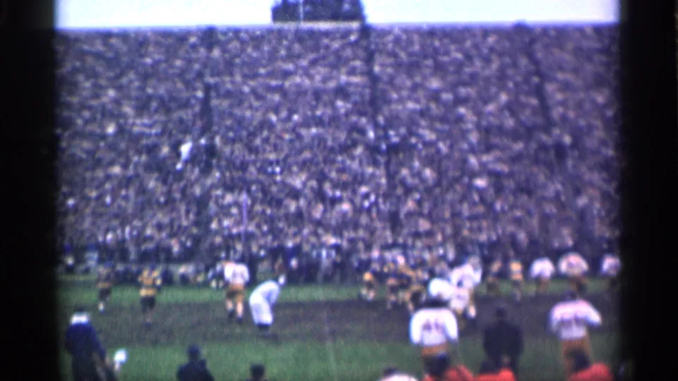 San Francisco 1944 home-movie frame showing football players on a muddy grass field with dense stadium seating behind them.