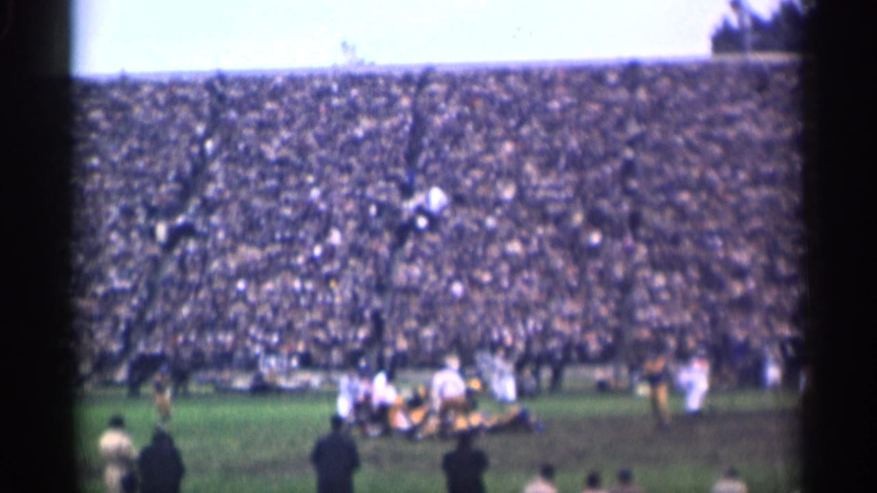 Players in white and dark uniforms pile up during a football play.