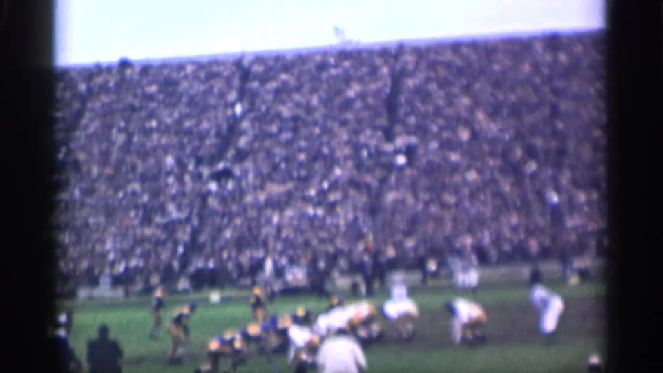 A 1944 San Francisco college football play begins, with players in motion near the line and a packed stadium behind them.