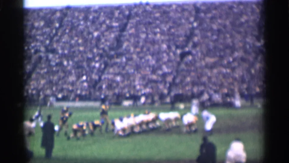 A sideline view shows the football formation from behind, with white and dark uniforms set against a large 1944 San Francisco crowd.
