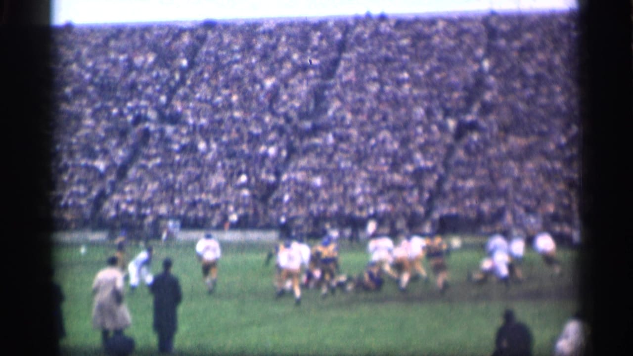 Football play on a grass field before packed stadium stands.