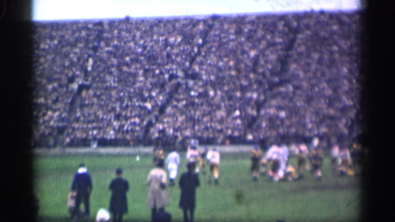 1944 San Francisco stadium view with football players in white and darker uniforms moving during play and adults standing along the sideline.