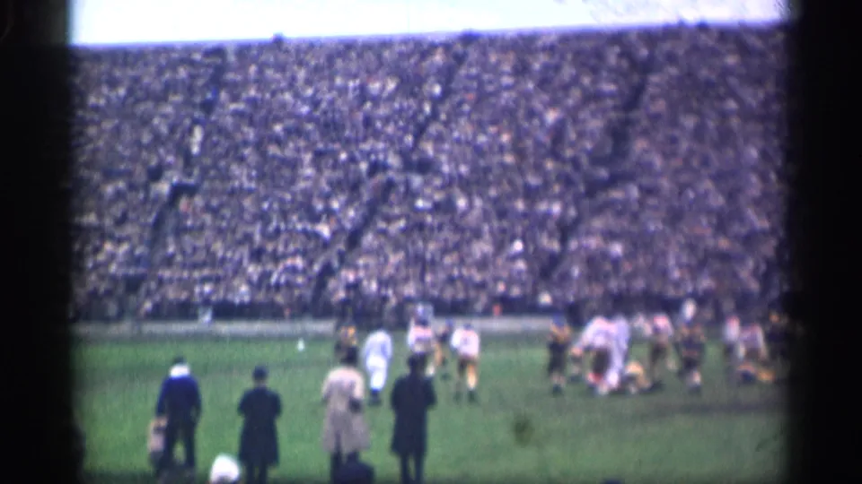 1944 San Francisco stadium view with football players in white and darker uniforms moving during play and adults standing along the sideline.