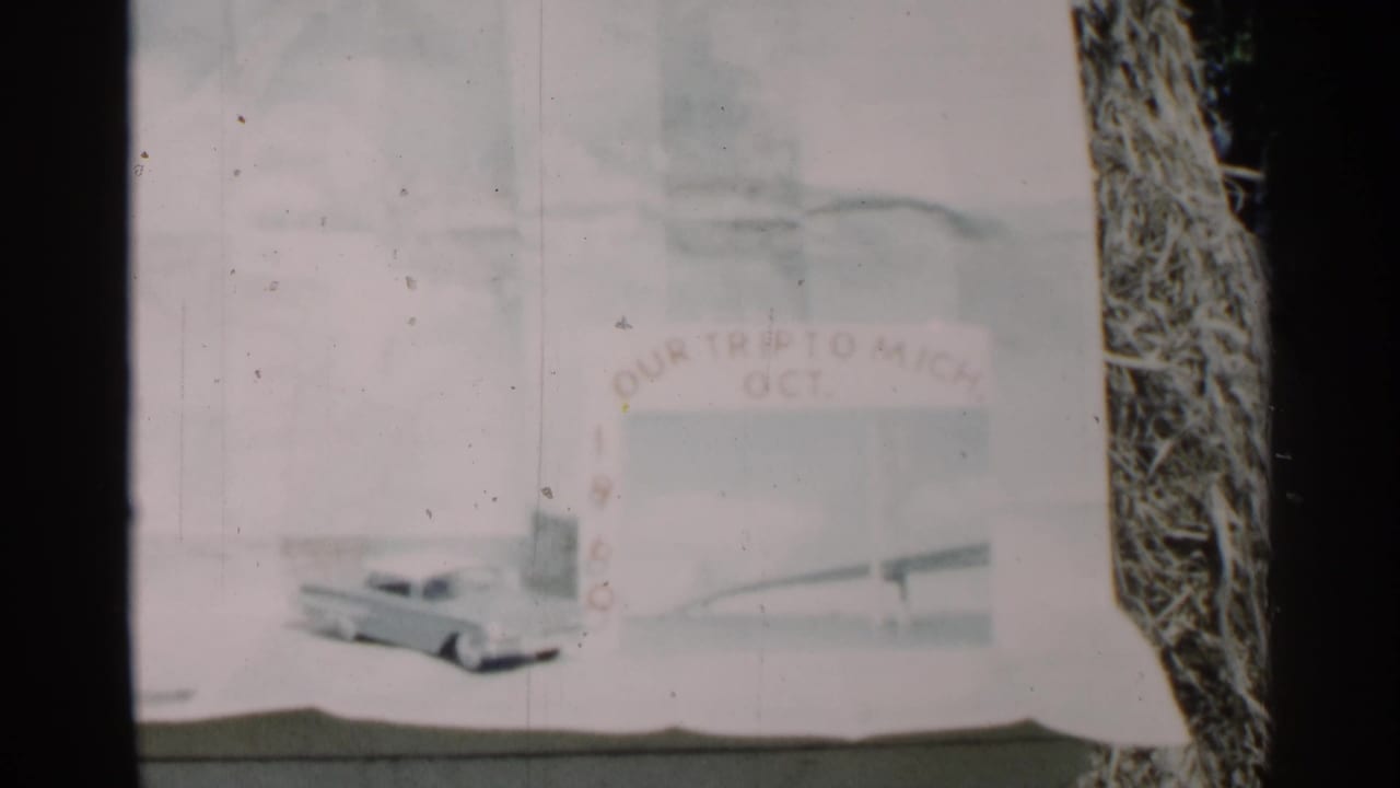 Soft 8mm frame of a handmade Michigan trip title card dated October 1960, with painted lettering and a bridge-like illustration.