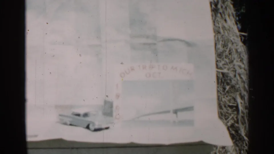 Soft 8mm frame of a handmade Michigan trip title card dated October 1960, with painted lettering and a bridge-like illustration.