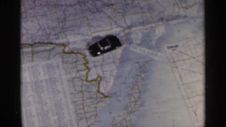 Toy car marker on a map of the Great Lakes region, used to visualize a Michigan road trip in 1960 home-movie footage.
