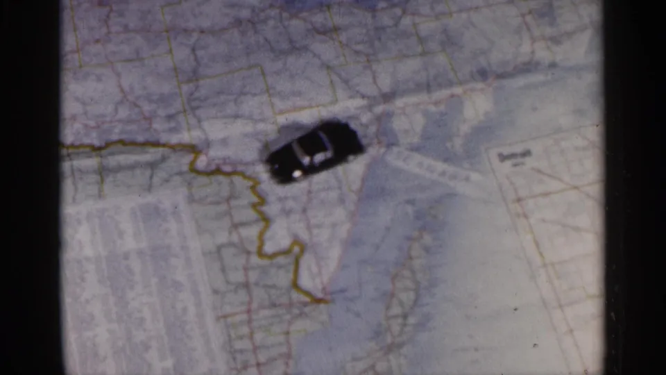 Close-up of the travel map and toy car marker, with faded color and soft 8mm texture visible in the frame.