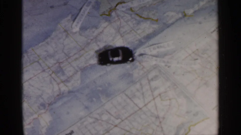 1960 8mm frame showing the toy car near printed Michigan map details, with soft focus and visible film borders.