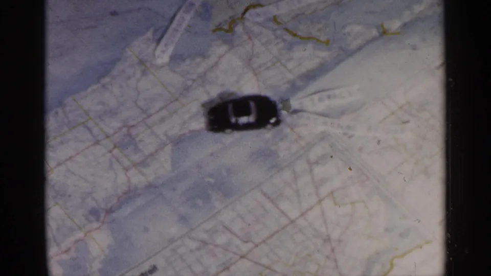 The toy car appears slightly shifted across the map, surrounded by pale blue-gray paper and fine colored route lines.