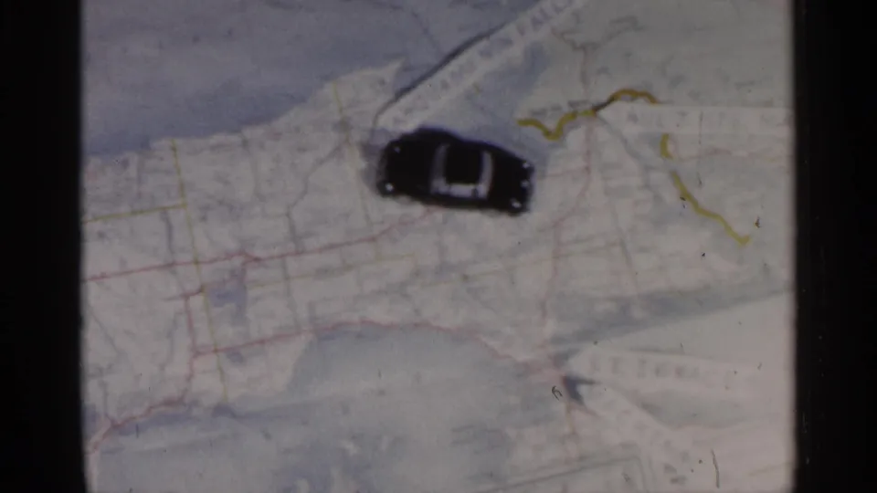 The small black car appears farther across the Michigan map, near drawn route marks and faint printed road lines.