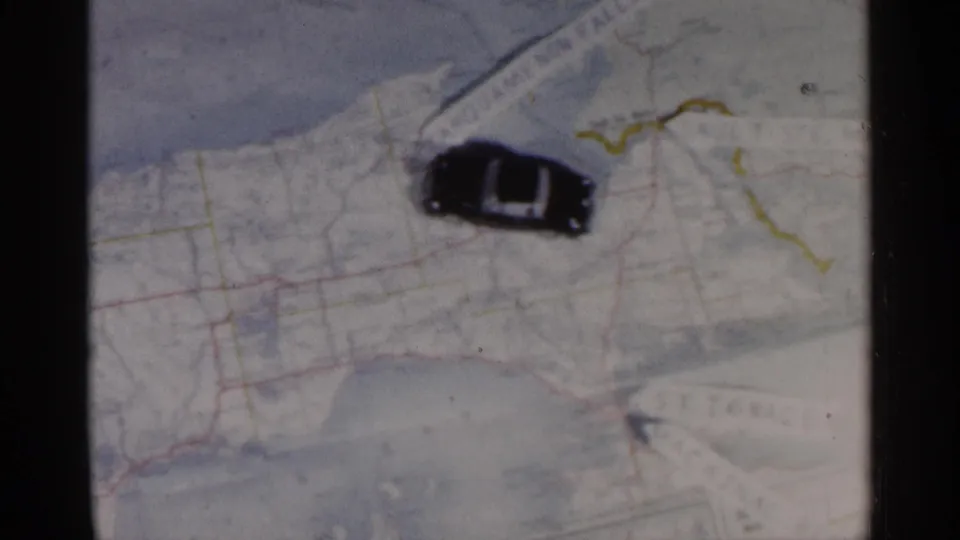 A black toy car rests over the Michigan map, with hand-marked lines and pale blue water shapes visible around it.
