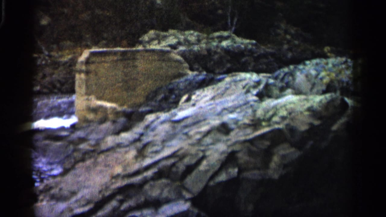 Rocky river edge with flowing water and a weathered concrete structure.