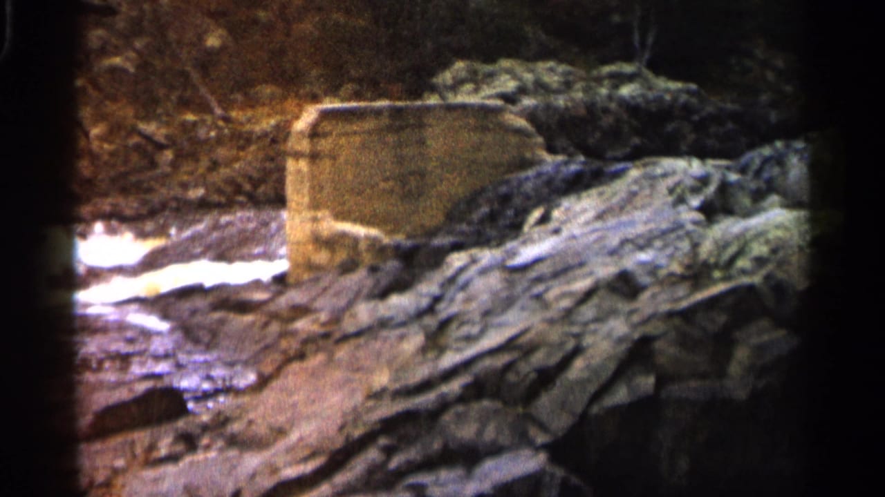 Concrete river structure above rocks with water passing behind it.